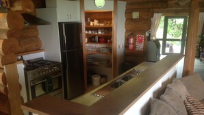 A kitchen with a stove, refrigerator, and wooden shelves with kitchenware. - Stunning Tidal Waters Loglodge (Tolaga Bay)