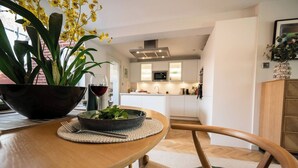 Un coin repas avec une table, des chaises, un saladier rempli de légumes verts, un verre à vin et une plante en pot.