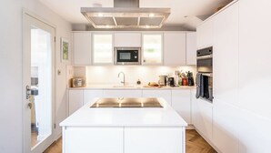 Une cuisine moderne avec des meubles blancs, un îlot central, un four à micro-ondes, un four et une hotte intégrée.