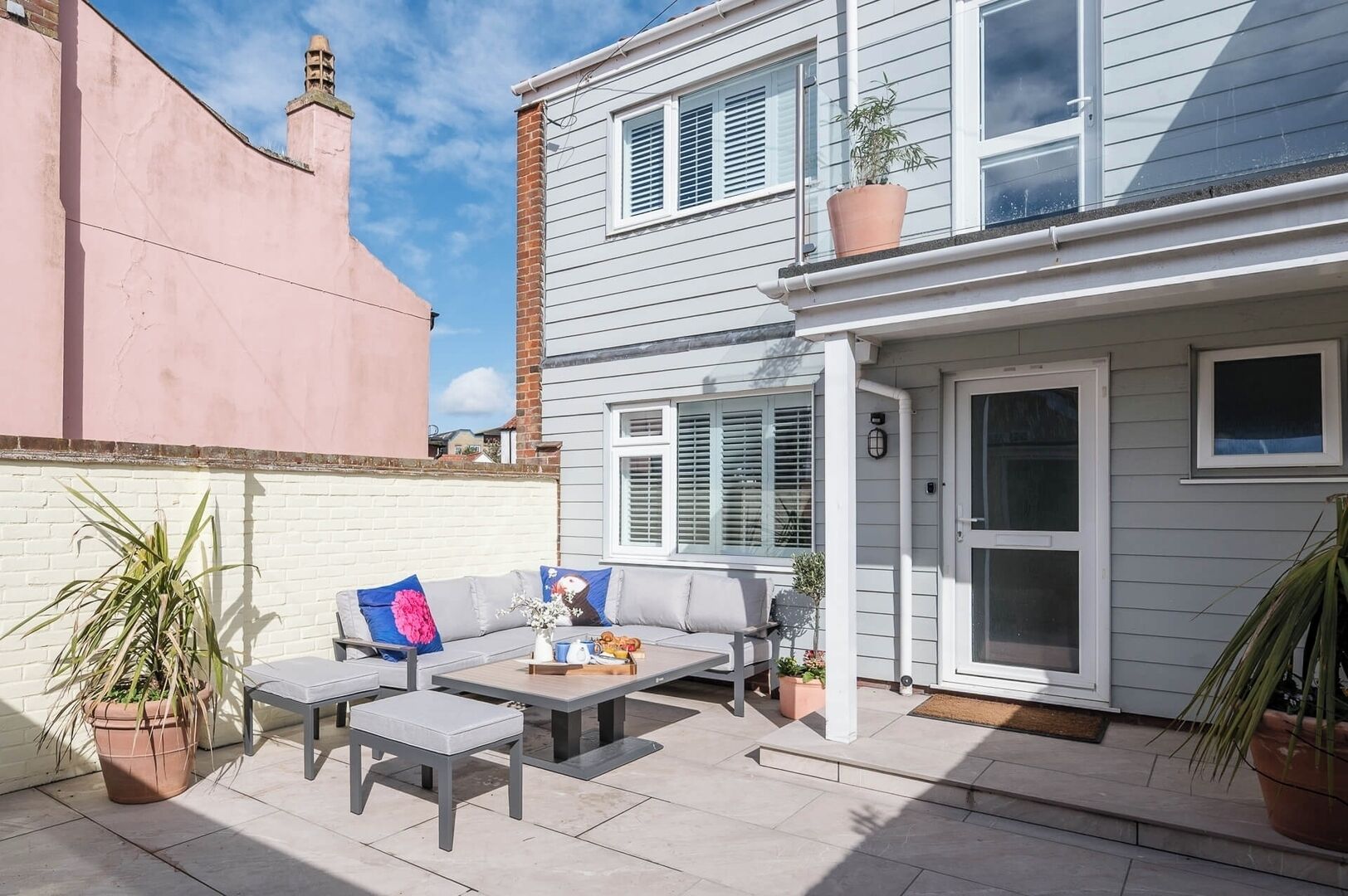 A patio with a sofa, table, and chairs, a potted plant, and a door to a house.