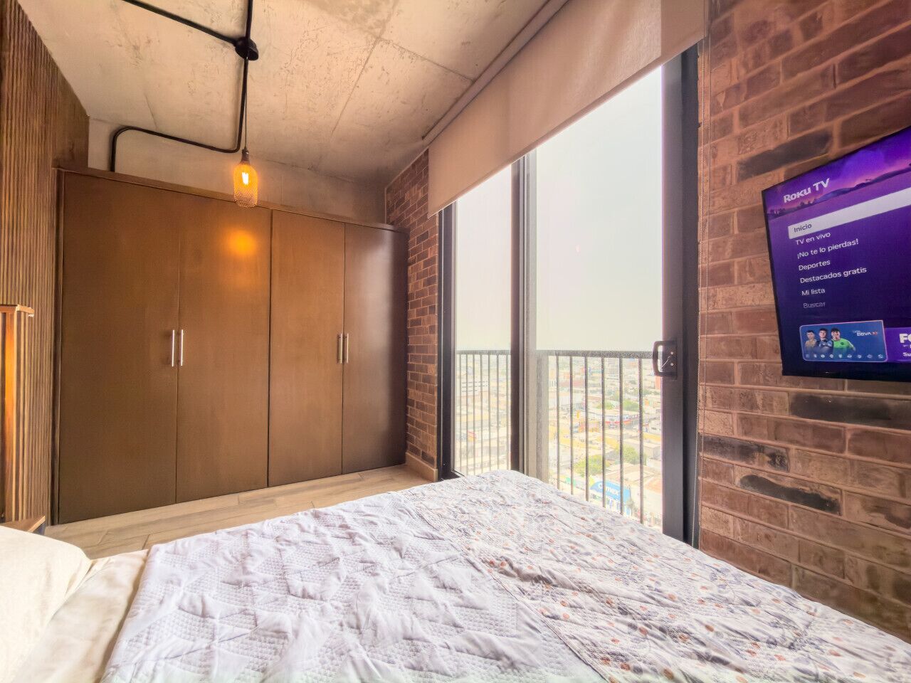 Une chambre avec un lit, une armoire, une télévision et un balcon offrant une vue sur la ville.