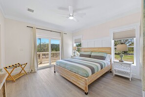 Une chambre à coucher comprenant un lit, un ventilateur de plafond, une table de chevet, une lampe, une fenêtre avec des stores et une porte-fenêtre donnant sur un balcon.