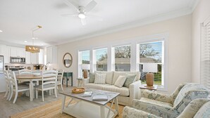 Ein modernes Wohnzimmer mit Essbereich, Deckenventilator und großen Fenstern mit Jalousien.