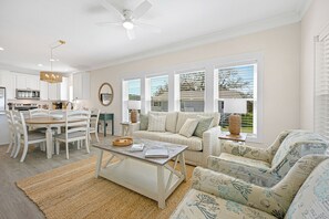 A modern living room with a dining area, a ceiling fan, and large windows with blinds. - Moon River, Waterfront Compound on Daufuskie Island (Daufuskie Island)
