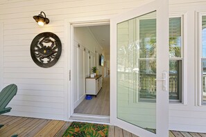 A house entrance with a door, a wall-mounted light fixture, a doorbell, a green chair, and a patterned rug. - Moon River, Waterfront Compound on Daufuskie Island (Daufuskie Island)