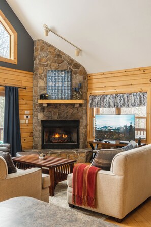 Una sala acogedora con chimenea de piedra, paredes de madera, televisor y asientos cómodos.