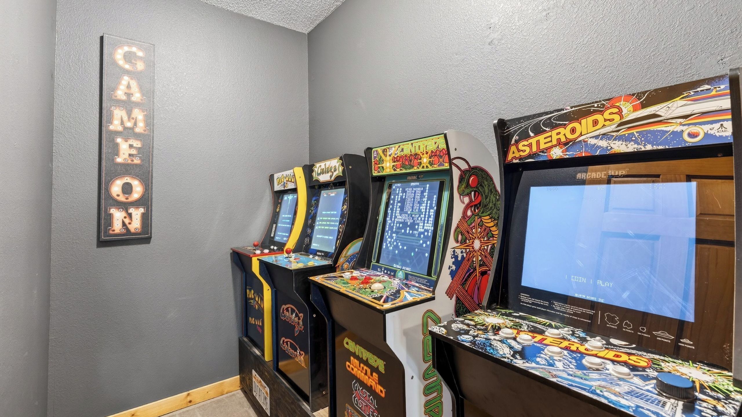 A row of arcade games in a room with a gray wall and a sign that reads 'GAME ON'.