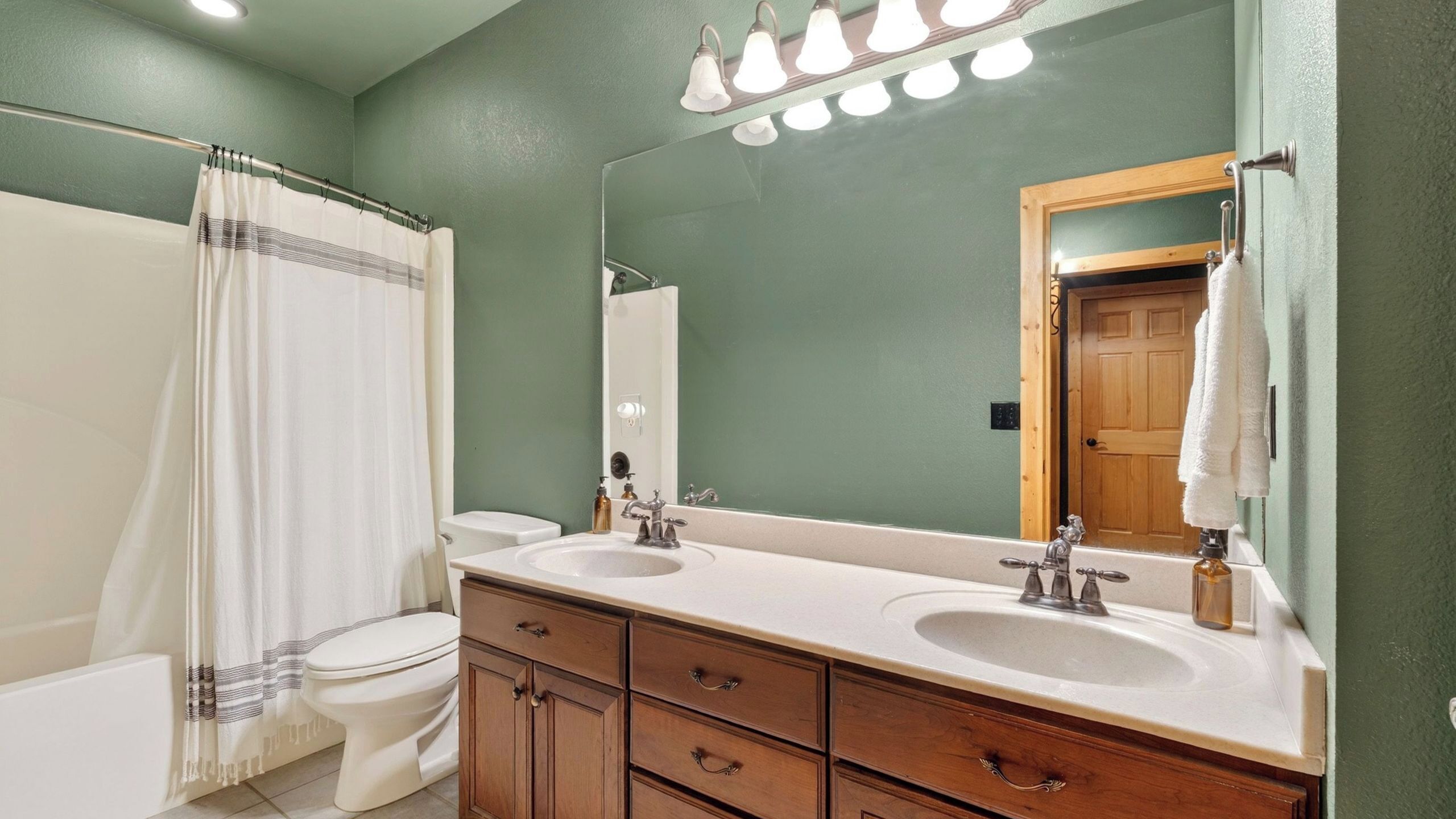 A bathroom with a double sink, a mirror, a shower curtain, and a toilet.