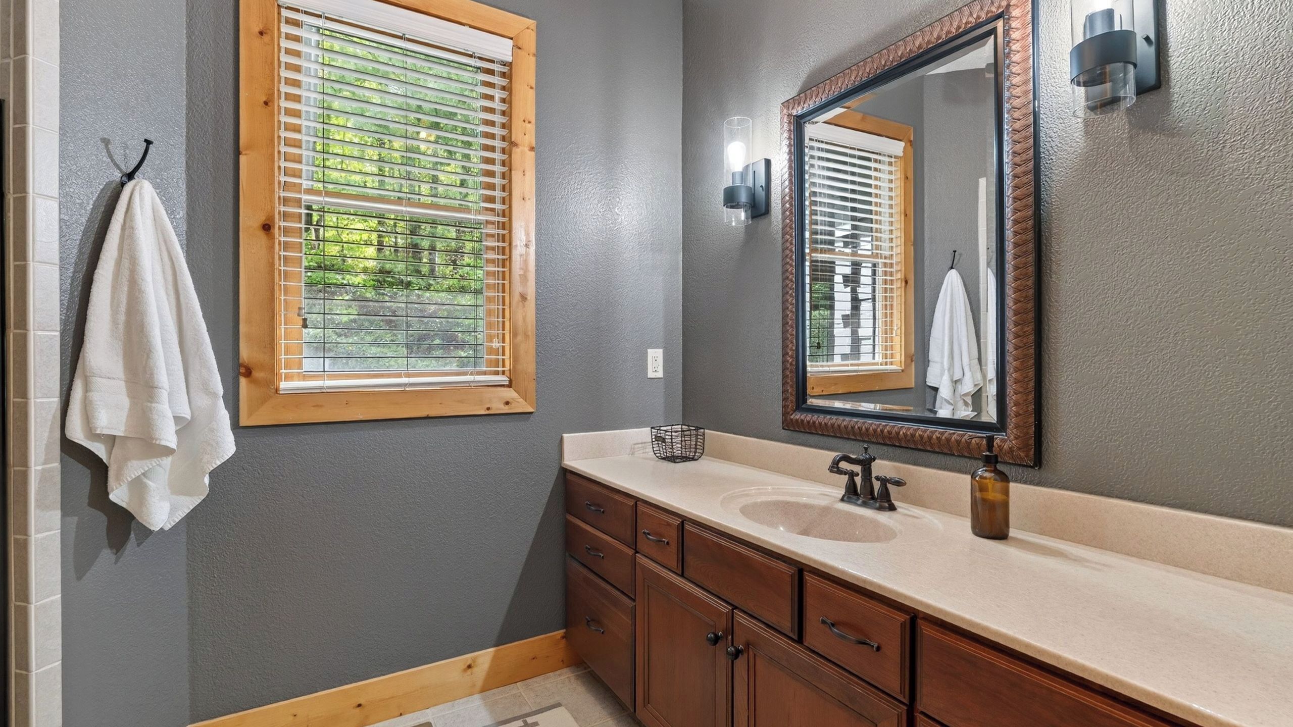 A bathroom with a wooden window, a large mirror, a sink, and a towel rack.