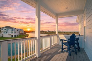 A covered porch with a view of a sunset over a body of water and houses. - Galveston 5BR Beach House | Lakefront | Sleeps 14 (Galveston)