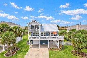A two-story house with a balcony, a garage, and a well-maintained lawn with palm trees. - Modern 3BR Galveston with Fire Pit & Private Pool & Jacuzzi | Mins to the Beach (Galveston)