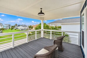 Eine überdachte Terrasse im Freien mit weißer Brüstung, zwei Korbstühlen und einem Tisch.
