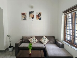A living room with a sofa, a coffee table with a plant, and three wall-mounted artworks.