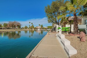A calm water body with a concrete walkway, palm trees, and a fence. - Fish and Kayak at The LAKE HOUSE (Peoria)