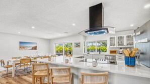 Una cucina moderna con mobili bianchi, un'isola grande con sgabelli da bar e vista sul verde circostante.