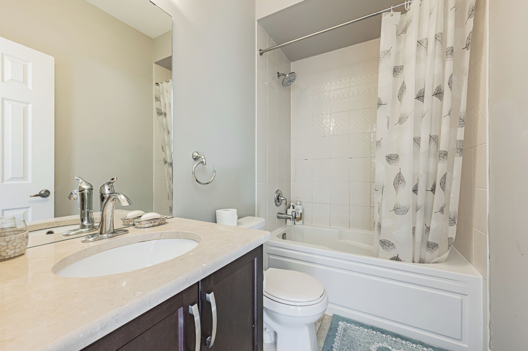A bathroom with two sinks, a toilet, a bathtub, and a shower curtain with a leaf pattern.