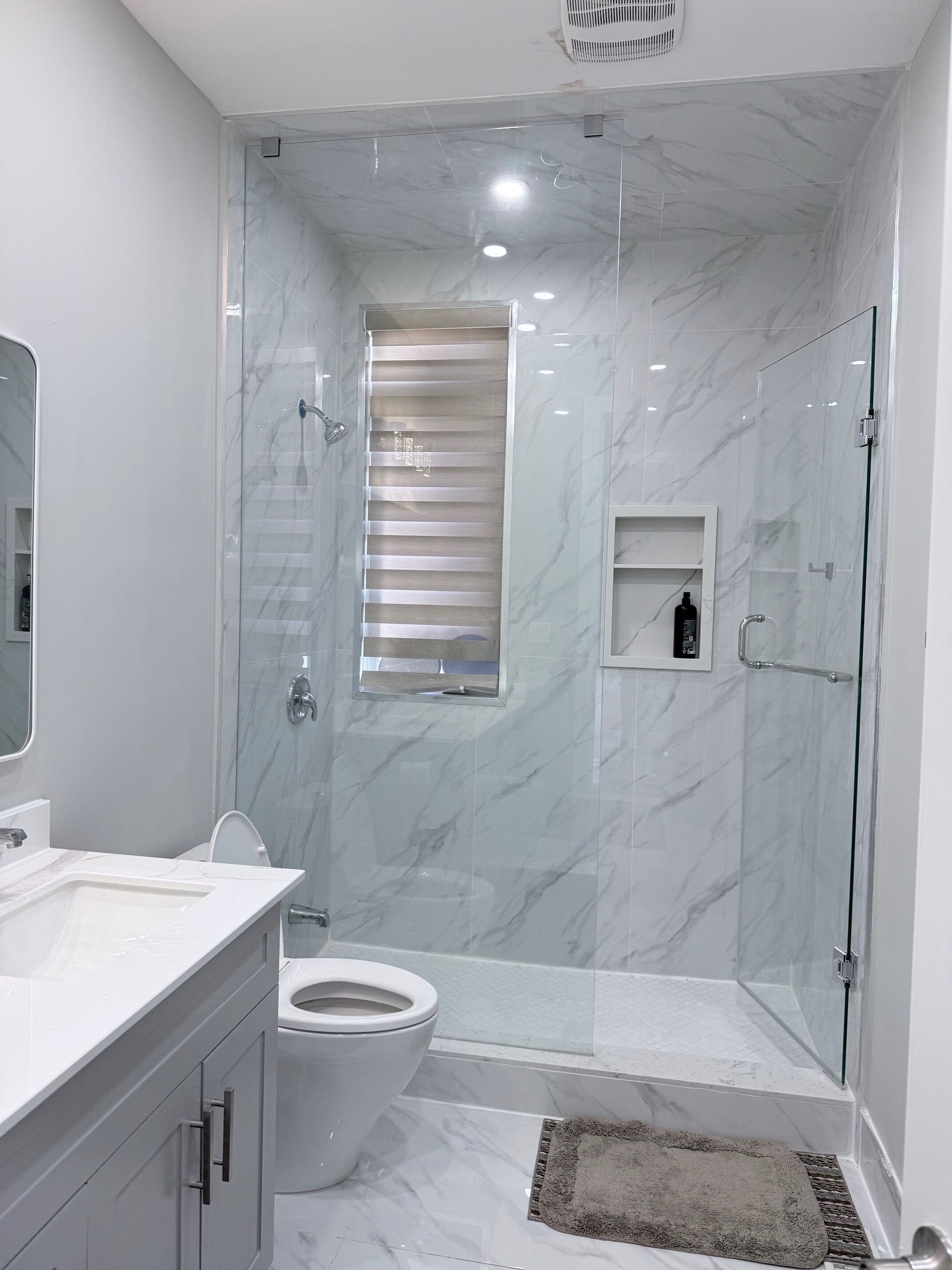 Een moderne badkamer met een douchecabine van glas, een toilet en een wastafel met spiegel.