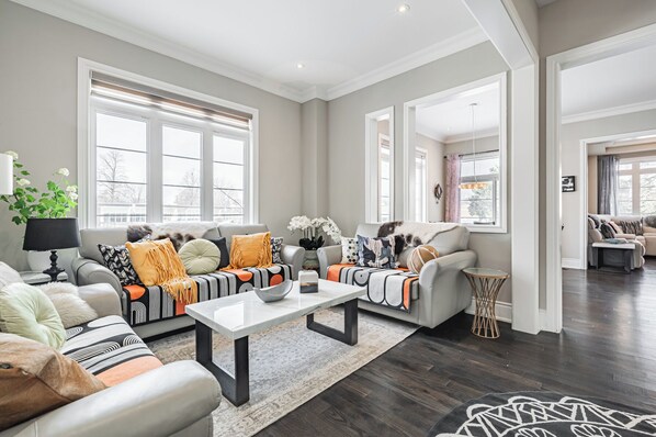 A spacious living room with a large window, a coffee table, and a sofa with various cushions.