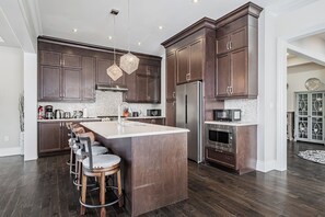 A spacious kitchen with dark wooden cabinets, a central island with bar stools, stainless steel appliances, and pendant lighting.