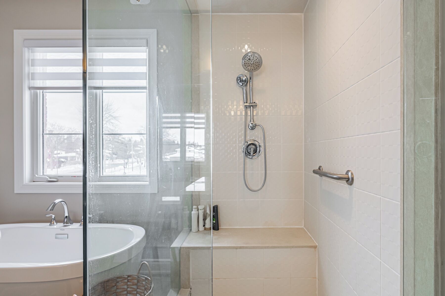 Une salle de bain avec une douche à parois de verre, une baignoire, un lavabo et une fenêtre avec des stores.