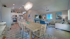 Un vaste espace de vie comprenant une table à manger en bois, des chaises en osier, un canapé et un téléviseur.