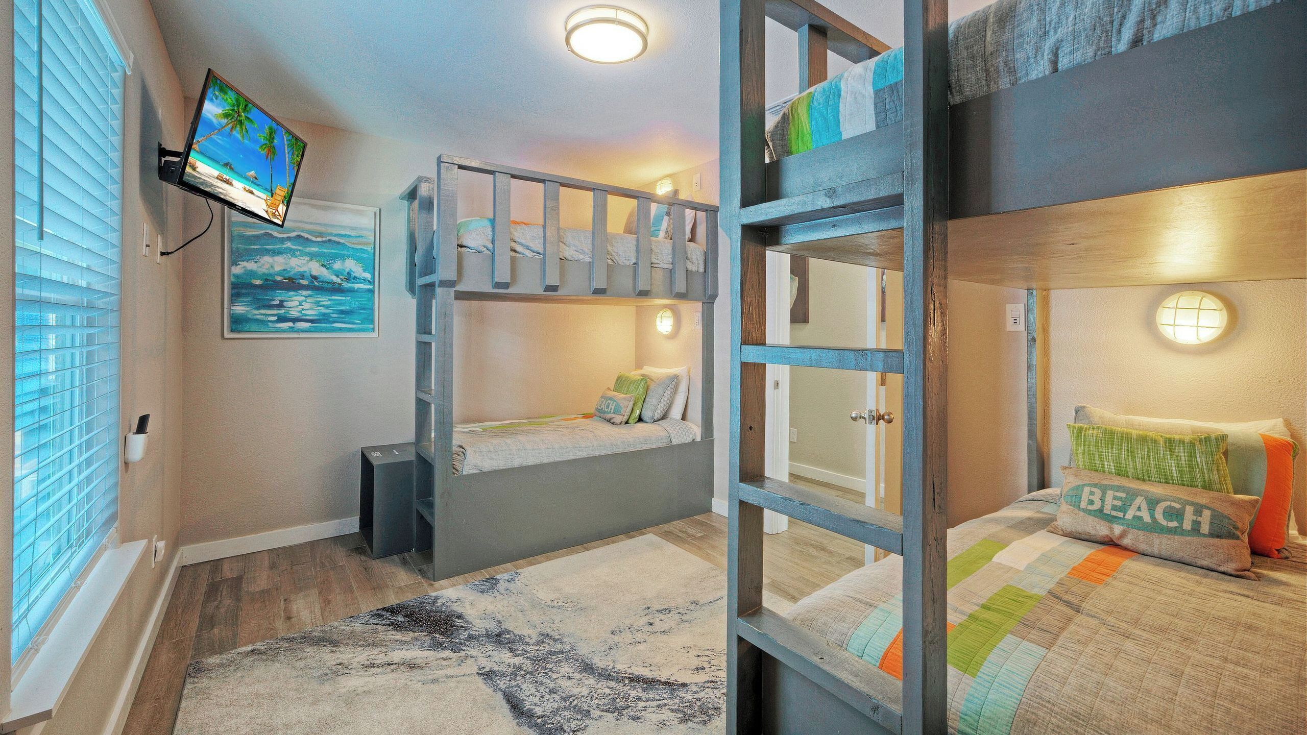A bunk bed room with a TV, a painting, and a beach-themed pillow.