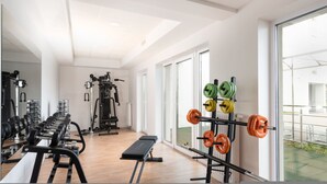 Un gimnasio con equipamiento para levantamiento de pesas, bancos y un ventanal grande.