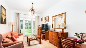 Una sala de estar con sofá, mesa de centro, televisor, armarios de madera y un comedor con sillas y una mesa.