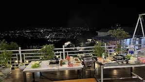 Un restaurante en la azotea con mesas al aire libre, una parrilla y vistas a un paisaje urbano nocturno.