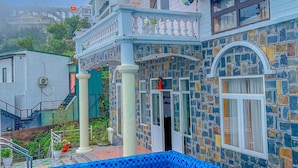 Una casa con piscina, fachada de piedra y un balcón con plantas en macetas.