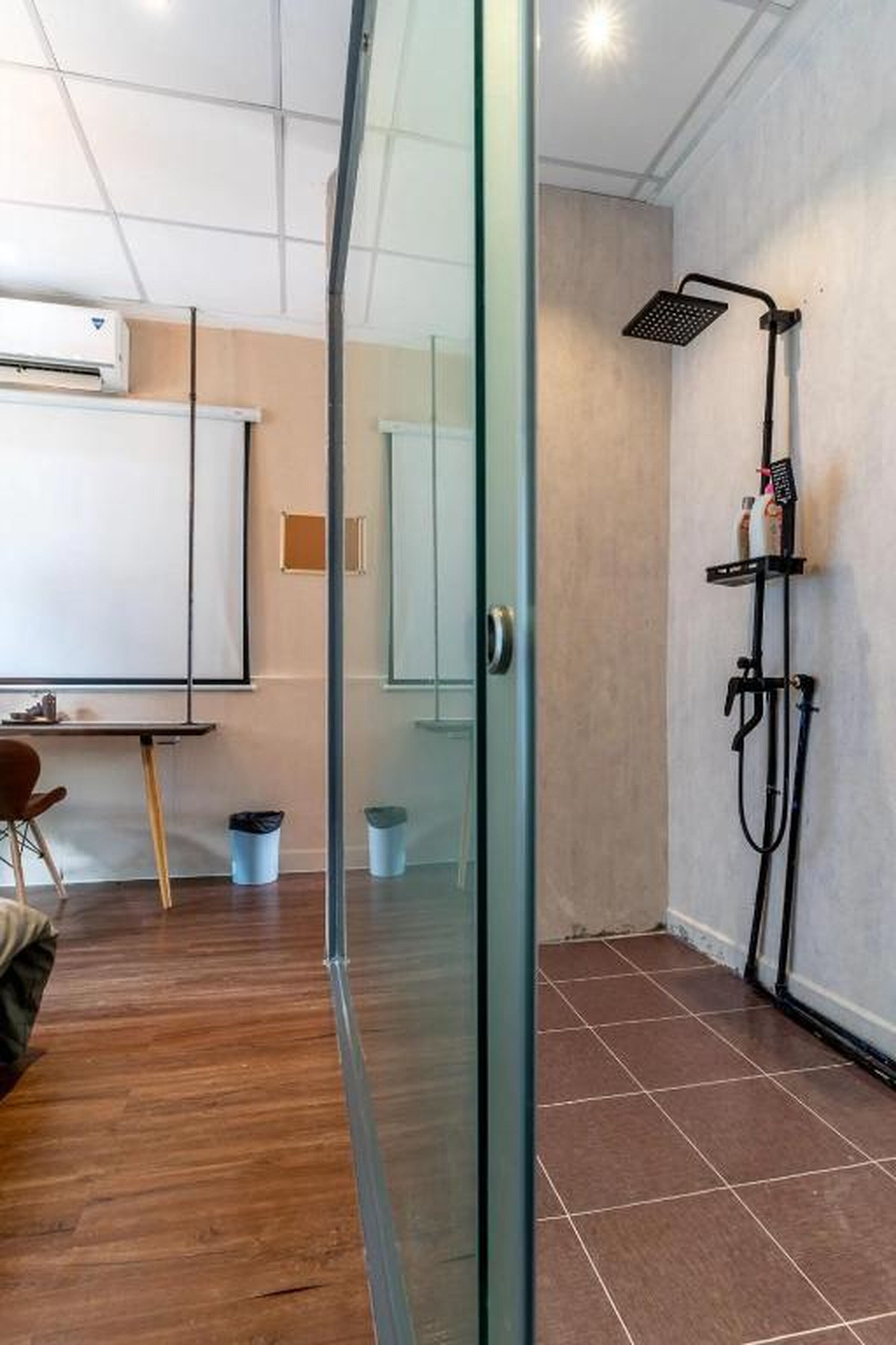Habitació amb separador de vidre, dutxa, pissarra i escriptori amb cadira.
