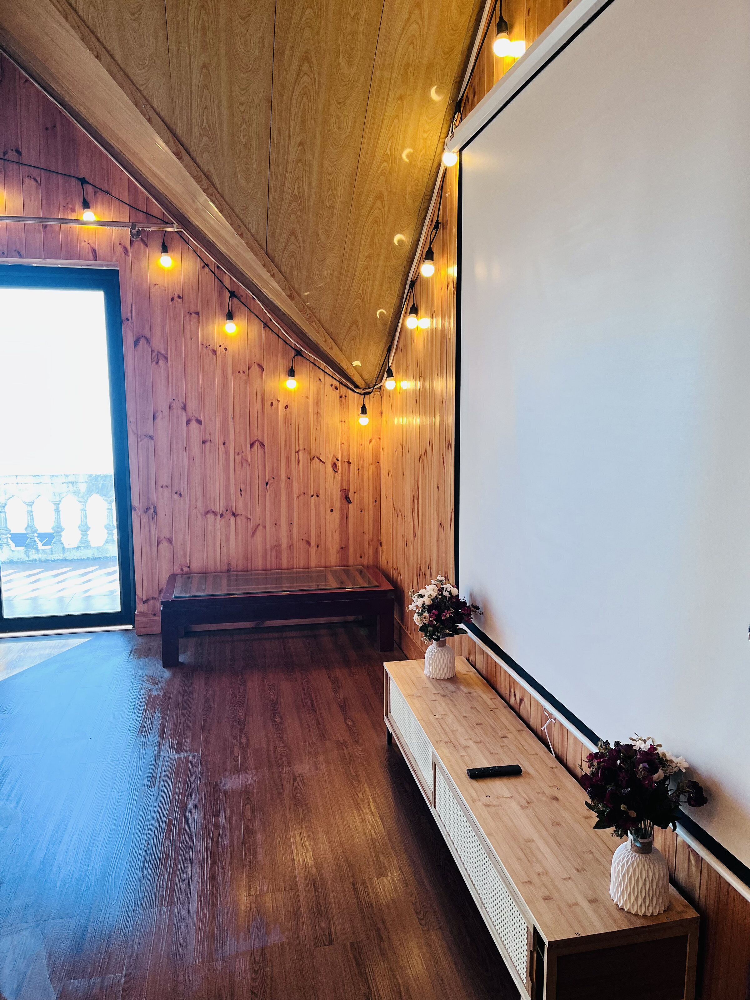 Una habitación con paredes de madera, un banco, una pizarra y una mesa de madera con un florero.
