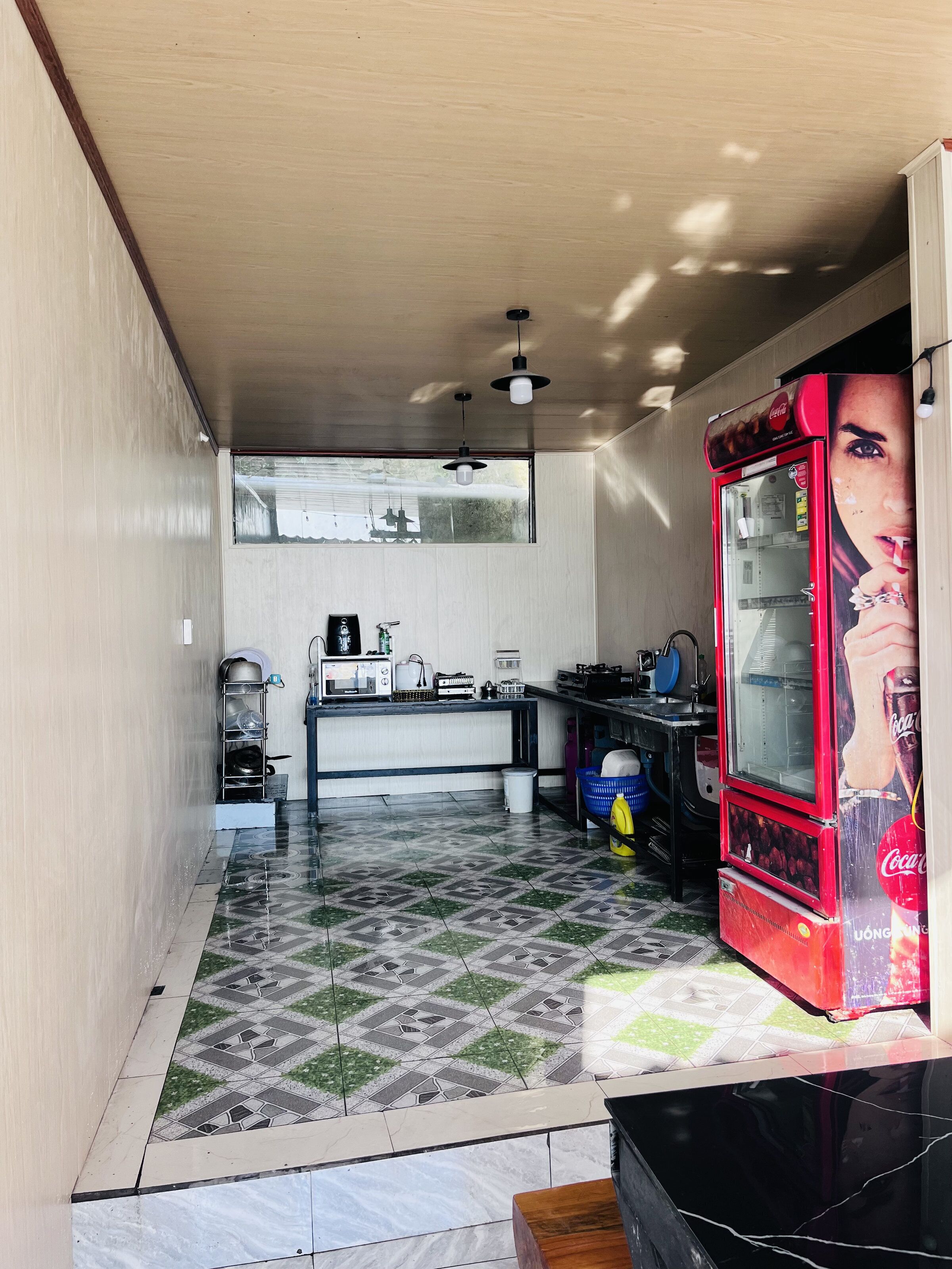 Una cocina con piso de baldosas, un refrigerador, un lavamanos y una ventana.