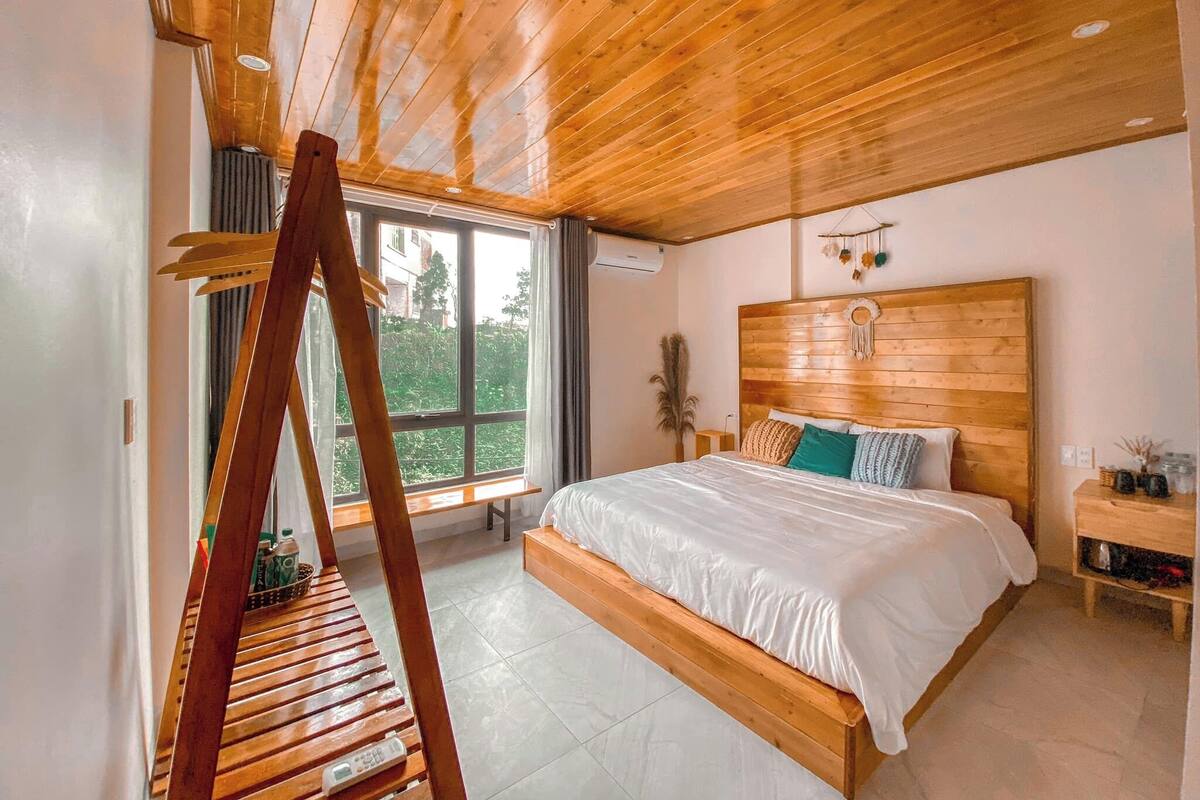 Ein Schlafzimmer mit Holzbalkendecke, einem großen Fenster, einem Bett mit weißer Bettwäsche und einem Nachttisch.