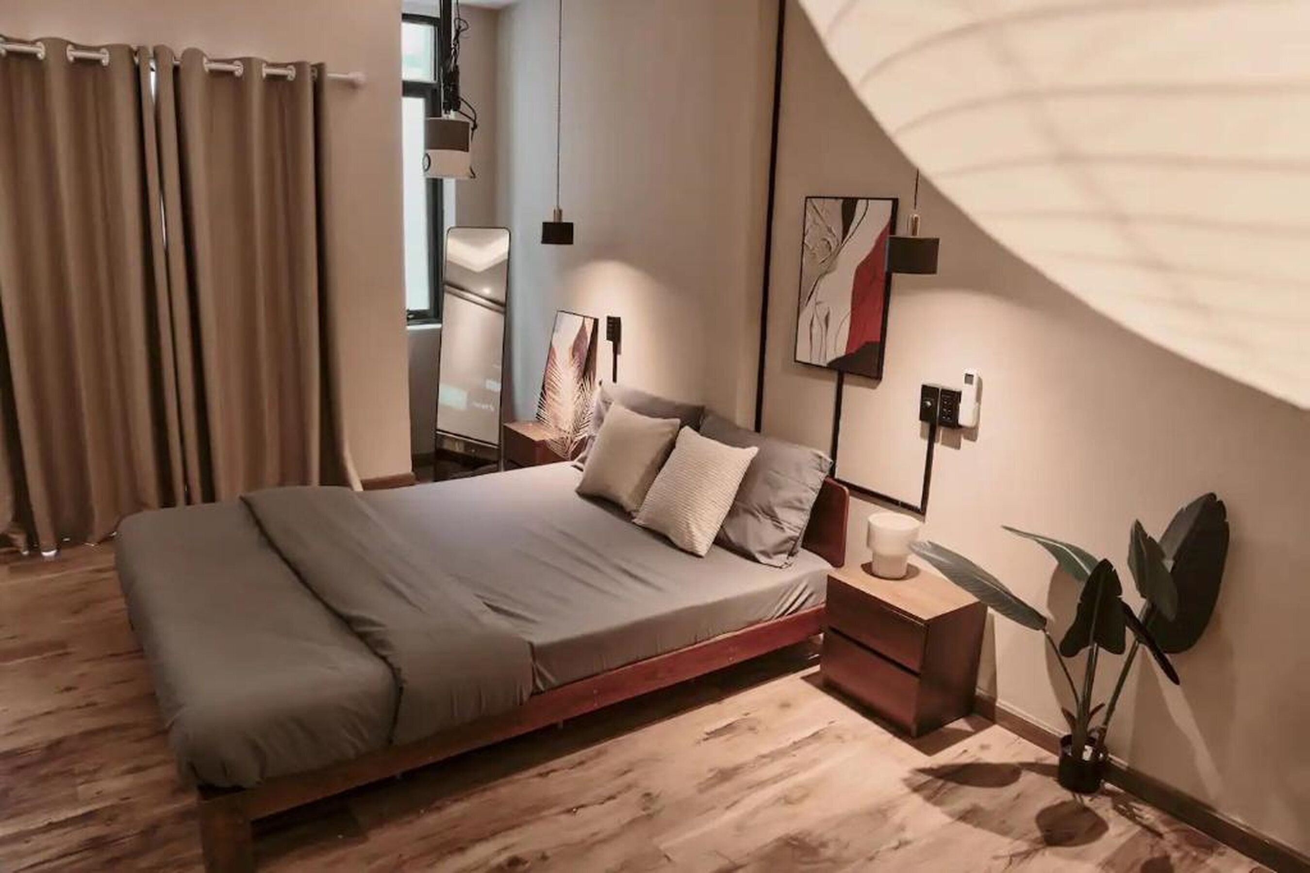 Un dormitorio moderno con cama, mesita de noche, lámpara y una planta en maceta.