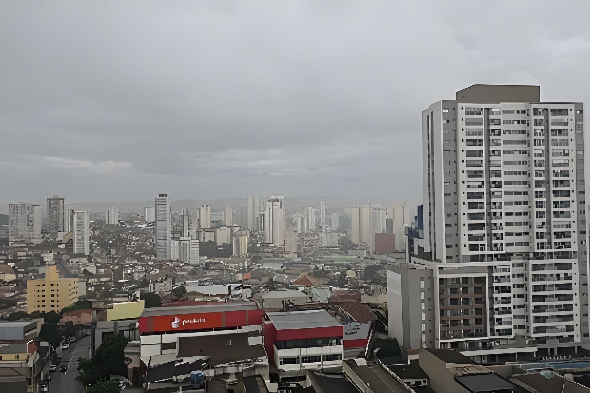 A cityscape with high-rise buildings, a prominent red and white building, and a cloudy sky.