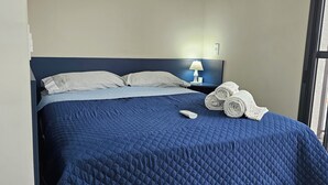 A hotel room with a bed, pillows, a remote control, and rolled towels. - Studios Expo Stay  (São Paulo)