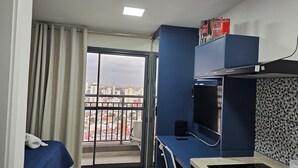 A hotel room with a balcony, a bed, a desk, and a TV. - Studios Expo Stay  (São Paulo)