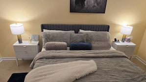 A neatly made bed with a grey headboard, two bedside tables with lamps, and a framed picture on the left table.
