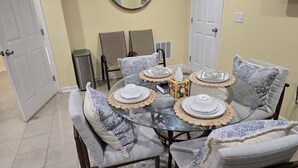 A dining table with four chairs, a glass top, and decorative plates.