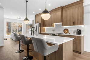 Una cucina moderna con mobili in legno, un'isola bianca e illuminazione a sospensione.