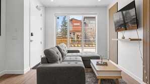 Uma sala de estar moderna com um sofá modular cinzento, uma mesa de centro de madeira e uma televisão de tela plana na parede.