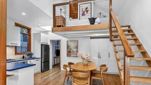 Eine moderne Küche mit Einbauherd, ein Essbereich mit rundem Tisch und Stühlen sowie eine Holztreppe.