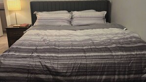 A bed with a striped comforter, a bedside lamp, and a dark headboard. - Room-standard Bedroom With King Size bed (Lethbridge)