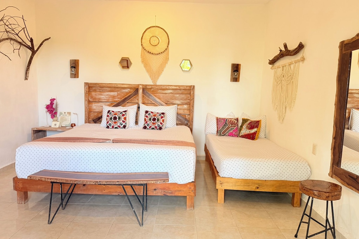A bedroom with a large bed, a smaller bed, a nightstand, a mirror, and a wall-mounted decorative item.
