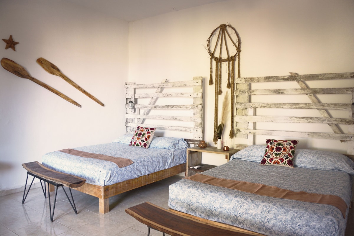 A room with two beds, a wooden bench, and a wall-mounted decoration.