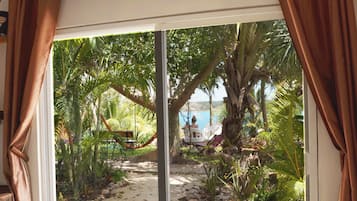 A room with a large sliding glass door leading to a tropical garden with palm trees and a view of the sea.