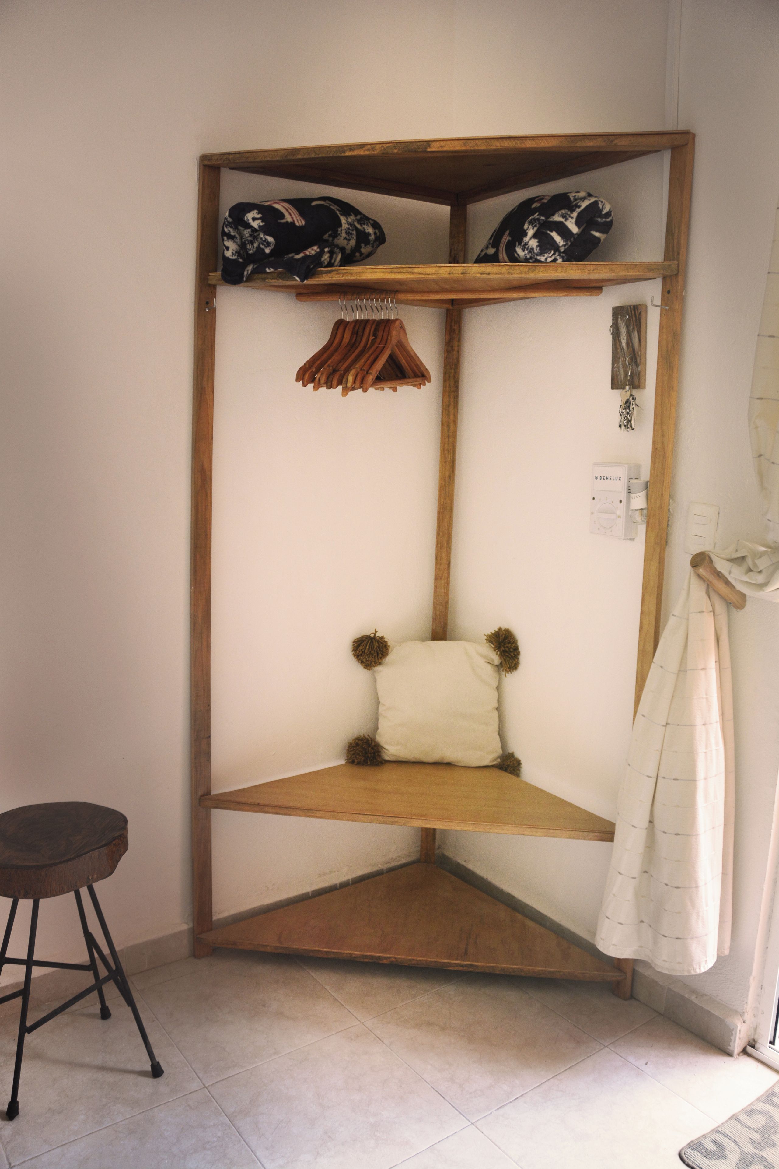 Habitación de esquina con un banco de madera, un perchero colgante y un pequeño estante con cojines estampados.