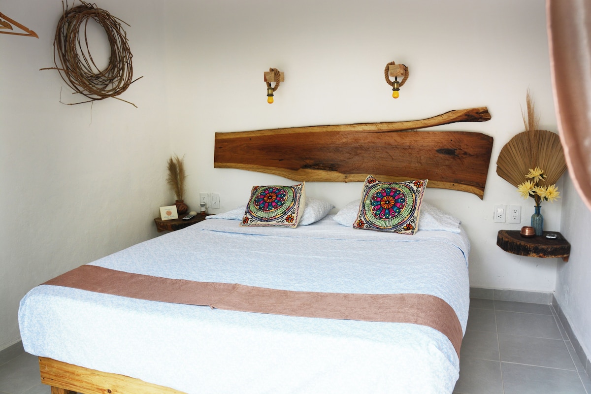 A bed with a wooden headboard, two decorative pillows, a bedside table with a vase and a phone, and a wall-mounted light fixture.