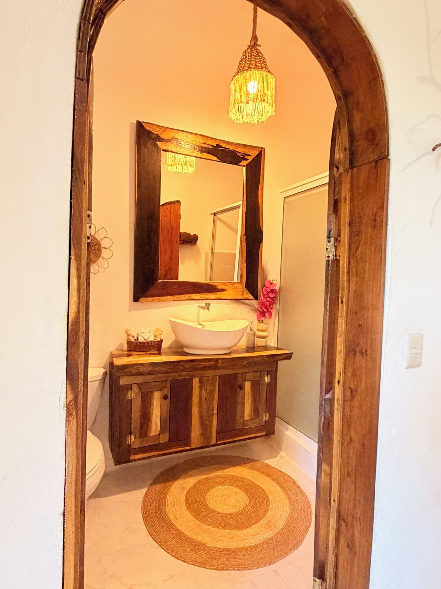 A bathroom with a wooden vanity, a white sink, a mirror, and a hanging light fixture.